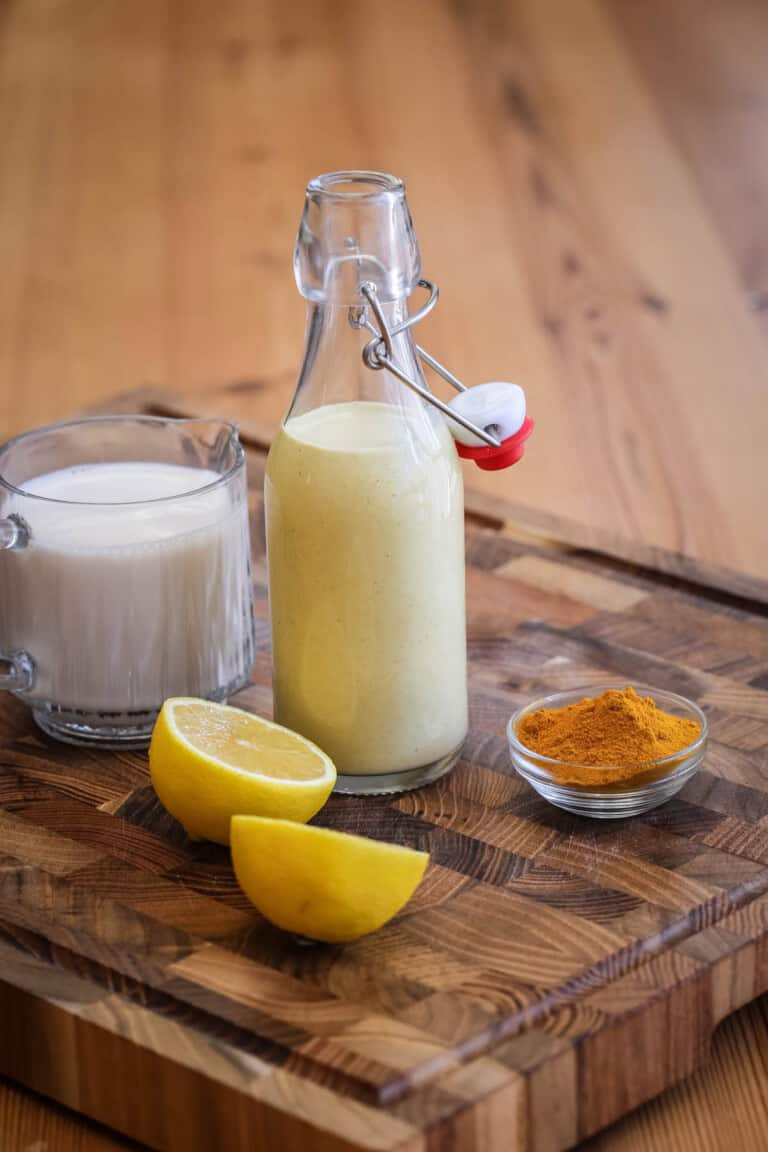 Tahini dressing in a clip top bottle surrounded by plant milk, lemon and turmeric.