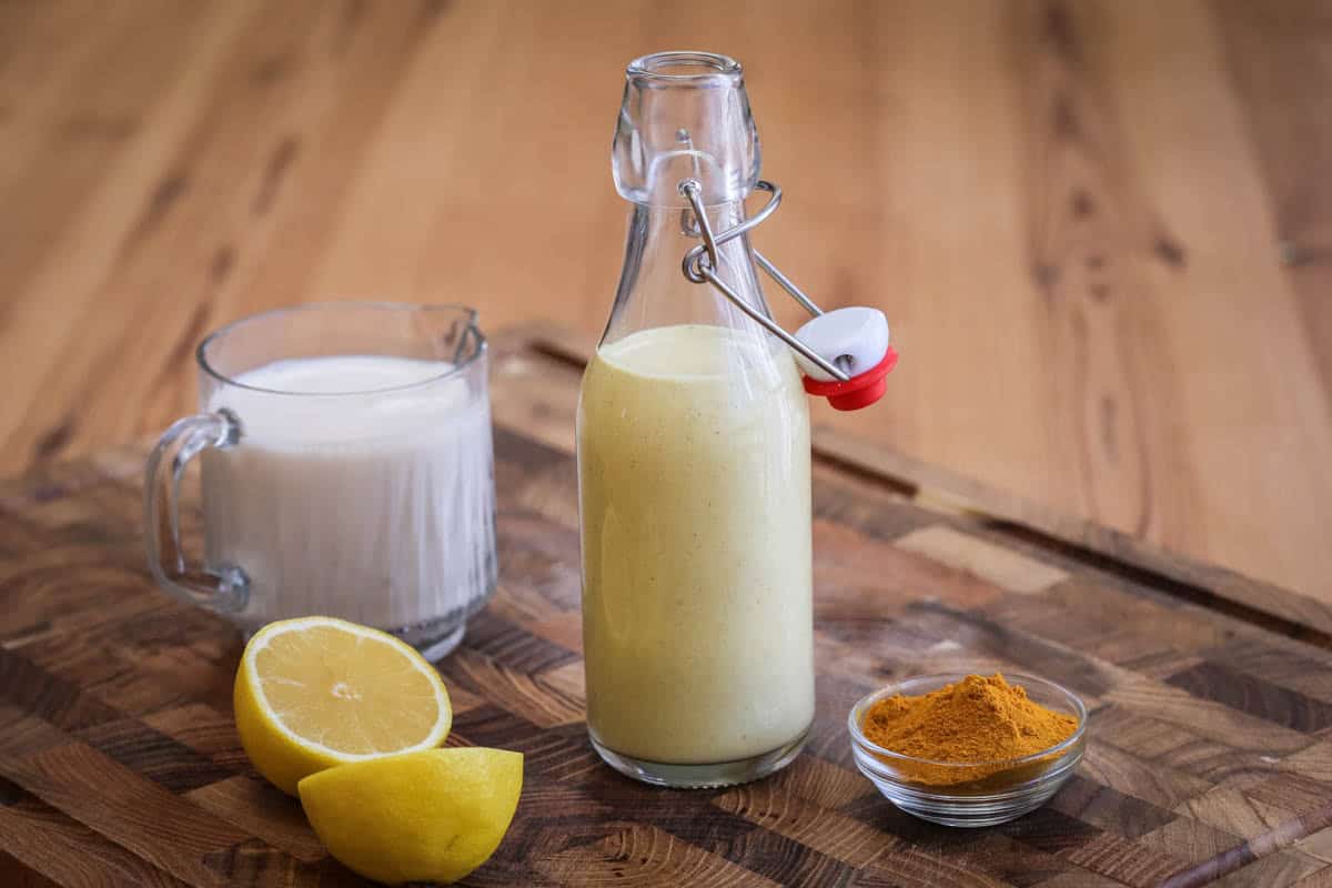 Tahini dressing in a clip top bottle surrounded by plant milk, lemon and turmeric.