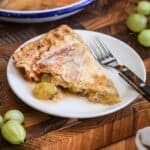 A slice of gooseberry pie on a plate showing crisp buttery pastry and a filling spilling out with juicy fruit.