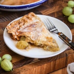 A slice of gooseberry pie on a plate showing crisp buttery pastry and a filling spilling out with juicy fruit.