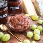 Gooseberry Chutney in a small dish, surrounded by fresh gooseberries and jars of chutney.