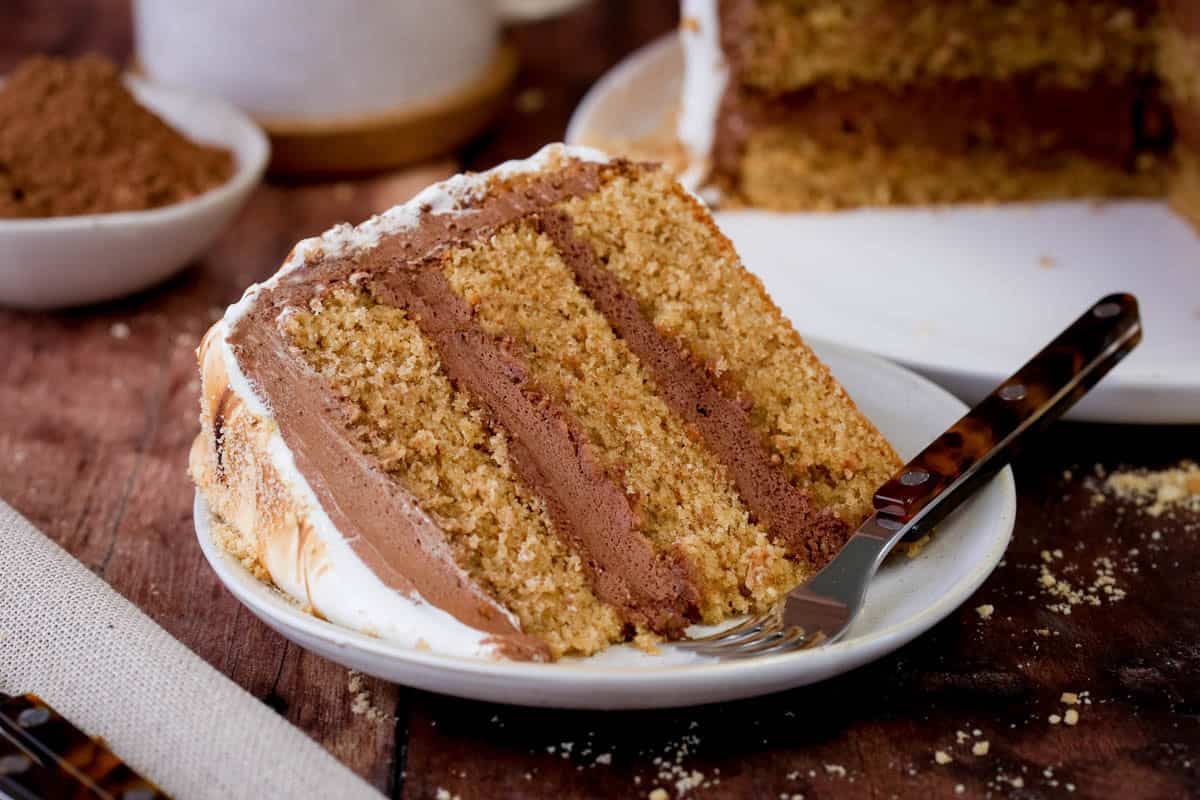 Cut slice of Gluten Free Smores Cake showing soft and tender cinnamon sponge, filled with ultra creamy chocolate filling and covered in toasted meringue.