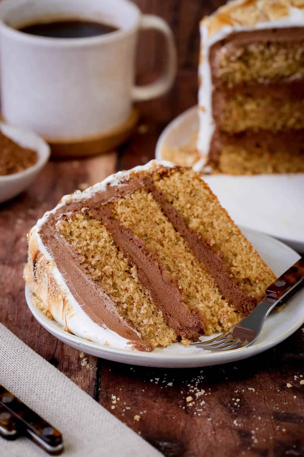 Cut slice of Gluten Free Smores Cake showing soft and tender cinnamon sponge, filled with ultra creamy chocolate filling and covered in toasted meringue.
