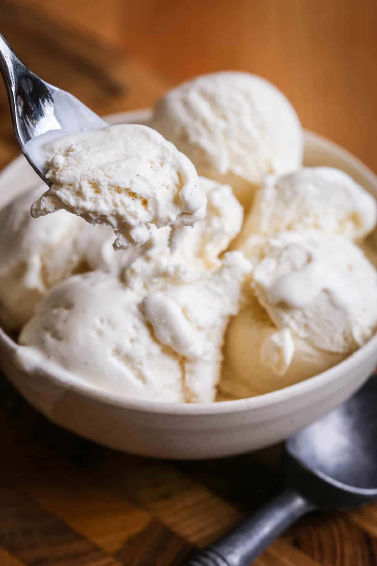 Gelato spoon scooping out vanilla ice cream from bowl.