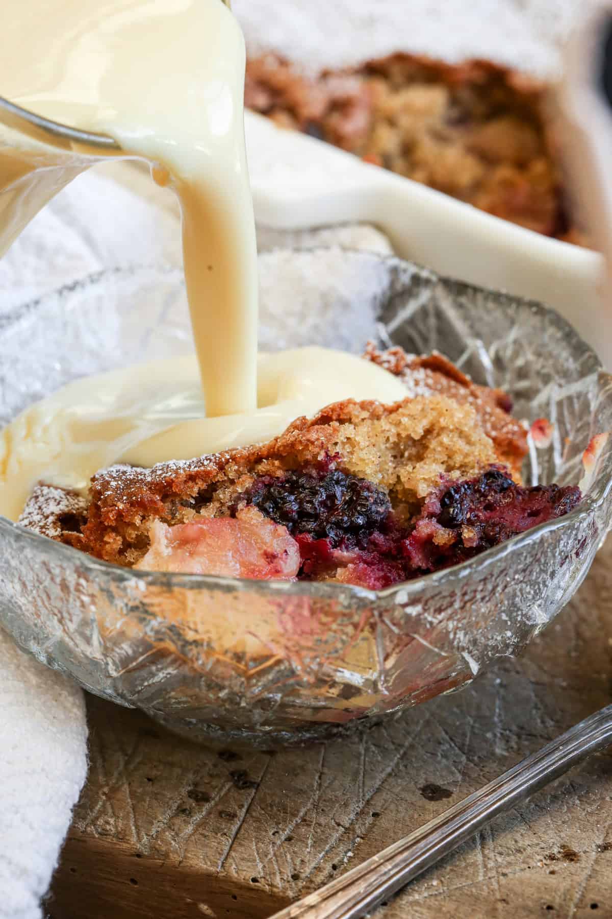 Custard pouring into bowl of Apple Blackberry Sponge.