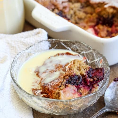 Bowl of Gluten-Free Blackberry Apple Sponge Pudding drenched in custard.