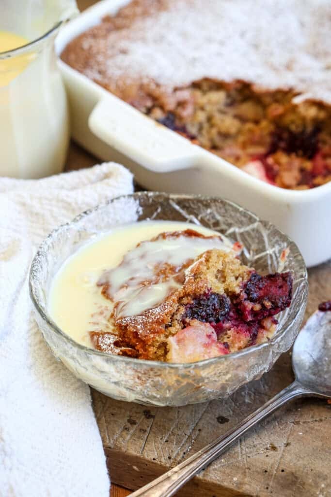 Bowl of Gluten-Free Blackberry Apple Sponge Pudding drenched in custard.