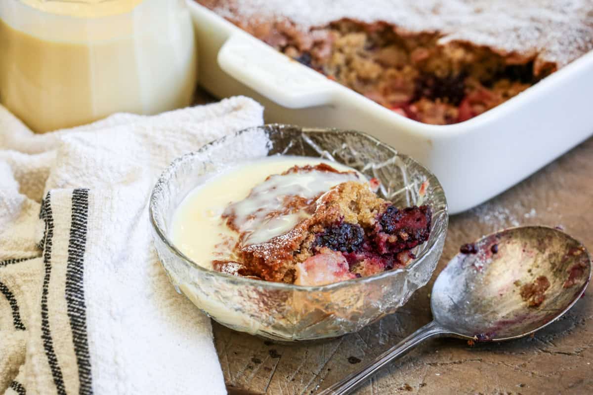Bowl of Gluten-Free Blackberry Apple Sponge Pudding drenched in custard.