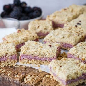 Gluten-Free Blackberry Bars on a wooden board with creamy blackberry cheesecake filling and buttery crumble layers.