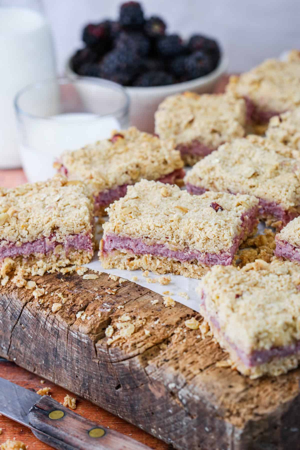 Gluten-Free Blackberry Bars on a wooden board with creamy blackberry cheesecake filling. Bowl of blackberries behind.
