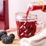 Beautifully claret coloured blackberry vinegar pouring from bottle into small jug.