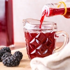 Beautifully claret coloured blackberry vinegar pouring from bottle into small jug.