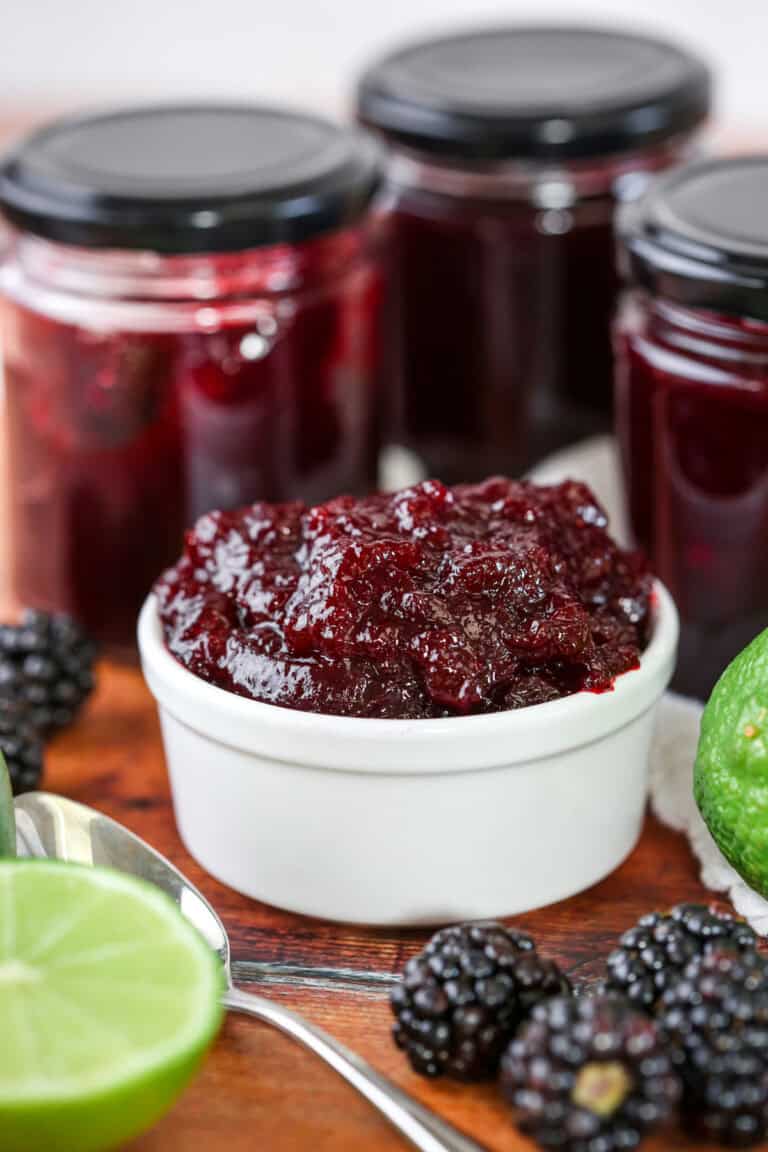 Blackberry Lime Jam in a pot surrounded by limes and blackberries.