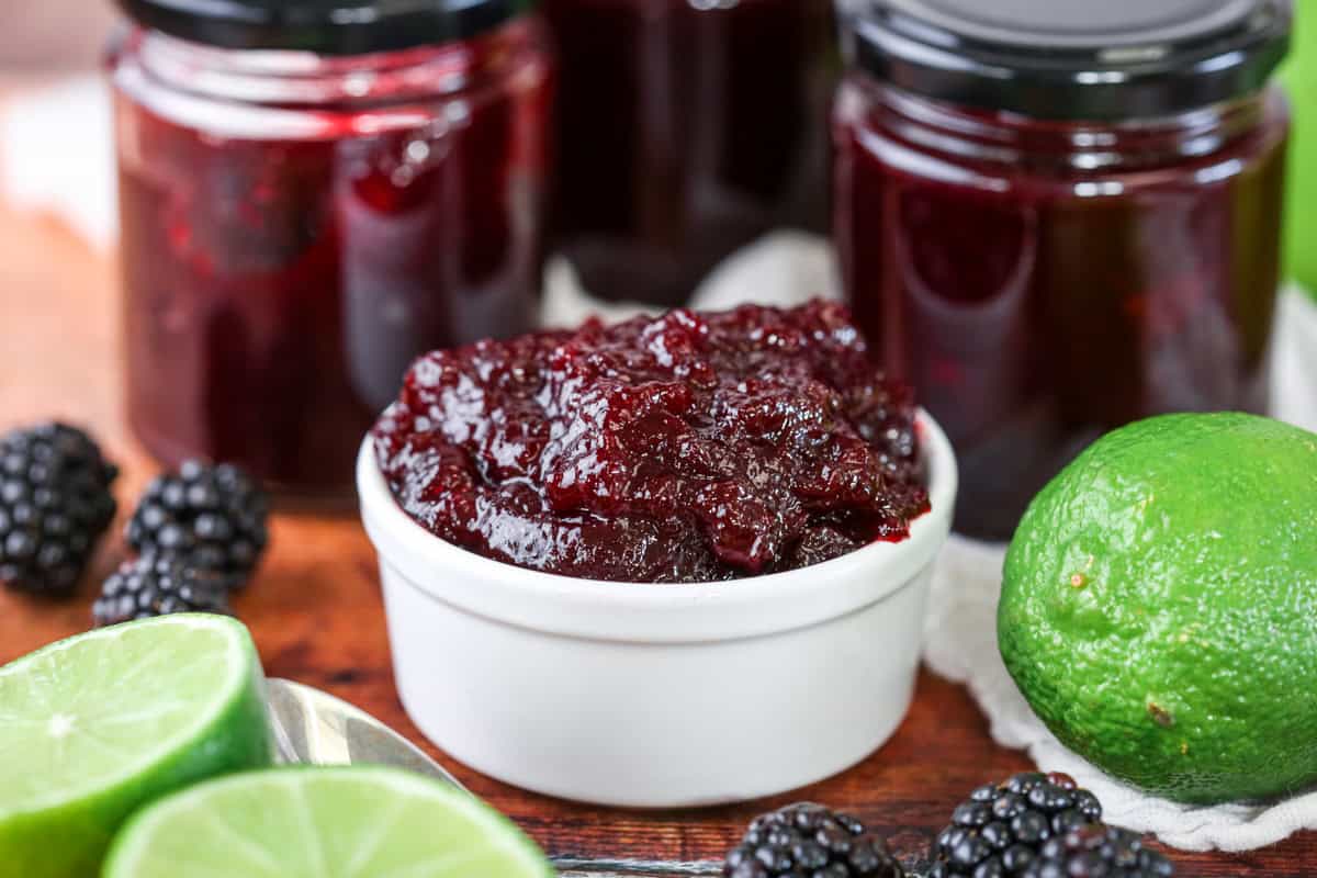 Blackberry Lime Jam in a pot surrounded by limes and blackberries.