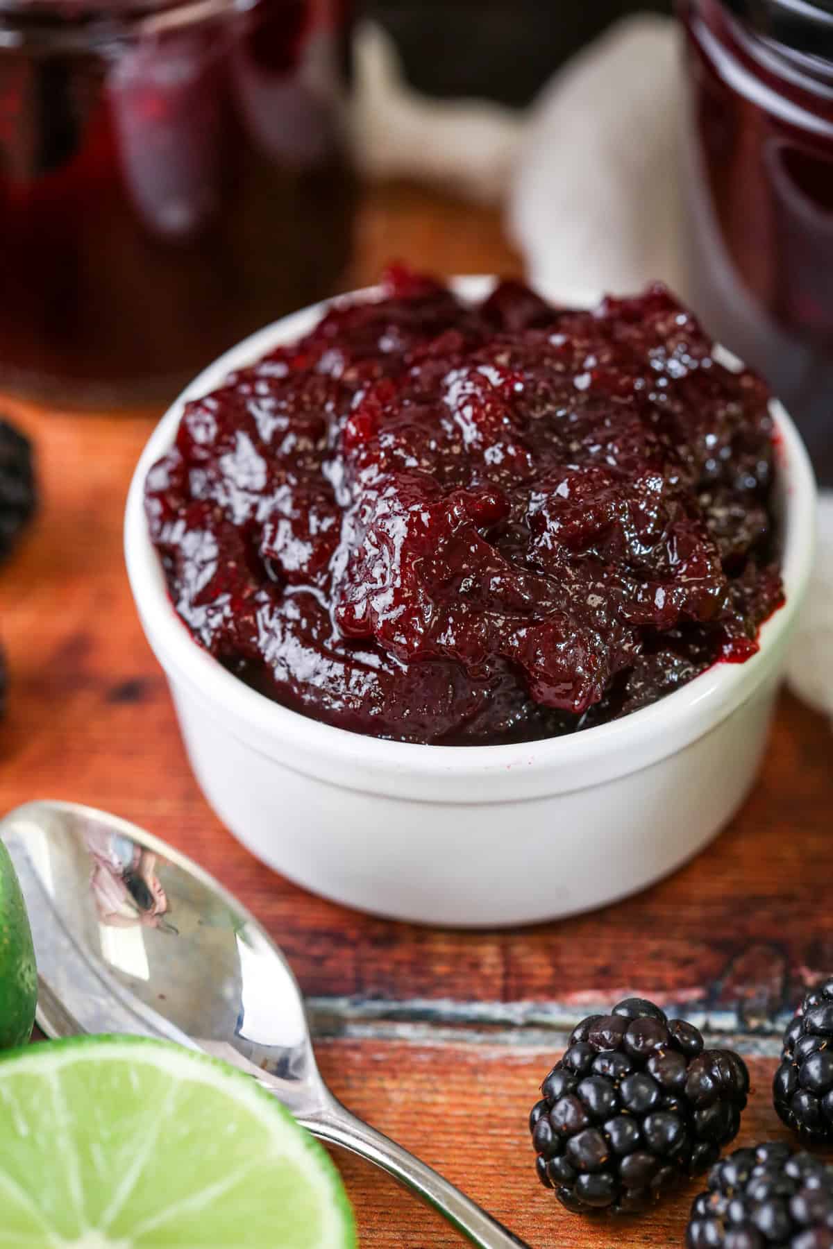 Blackberry Lime Jam in a pot surrounded by limes and blackberries.