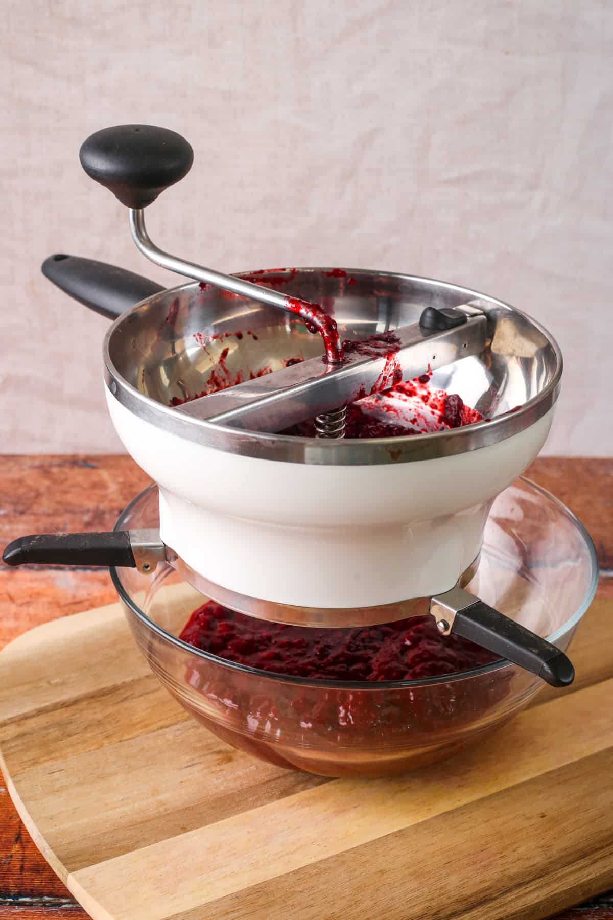 Softened blackberry and apple processed through food mill with smooth fruit pulp collected in glass bowl below.