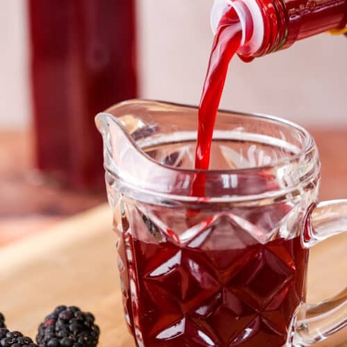 Beautifully claret coloured blackberry vinegar pouring from bottle into small jug.