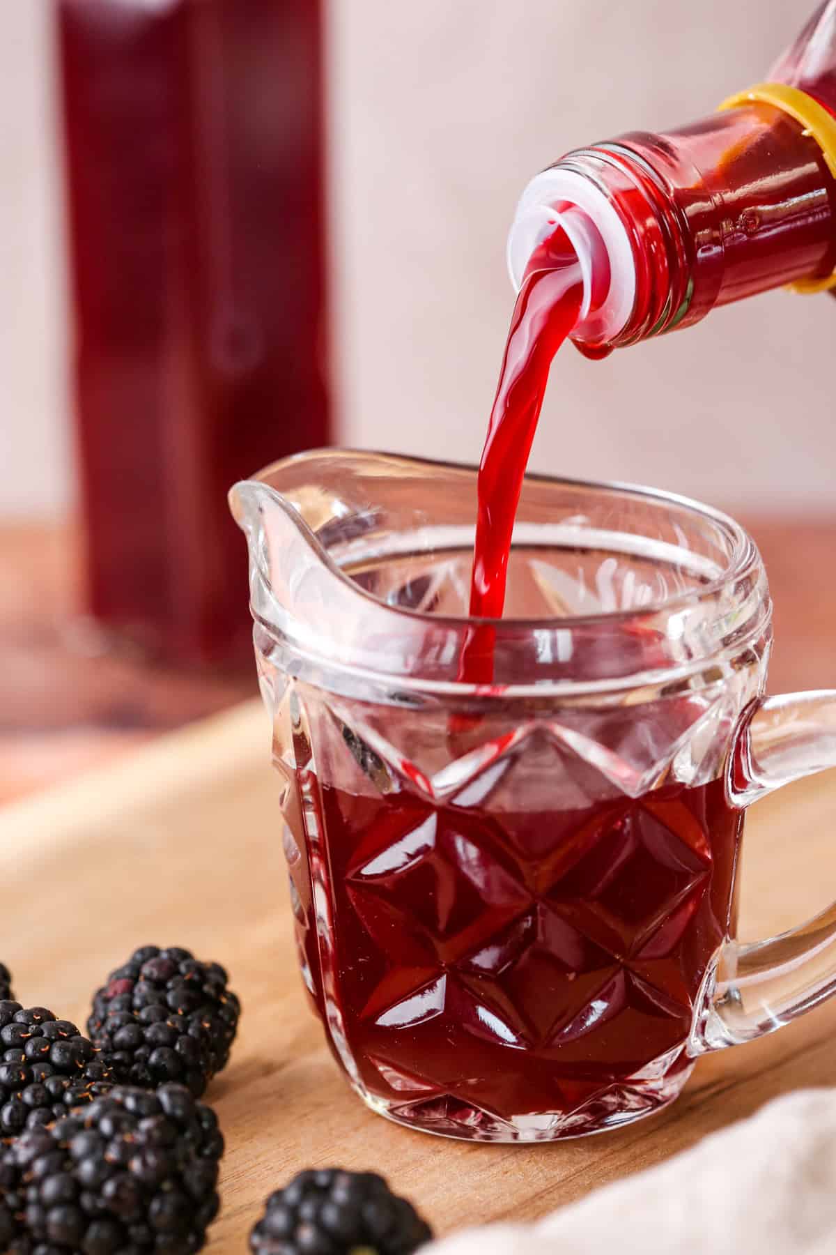 Beautifully claret coloured blackberry vinegar pouring from bottle into small jug.