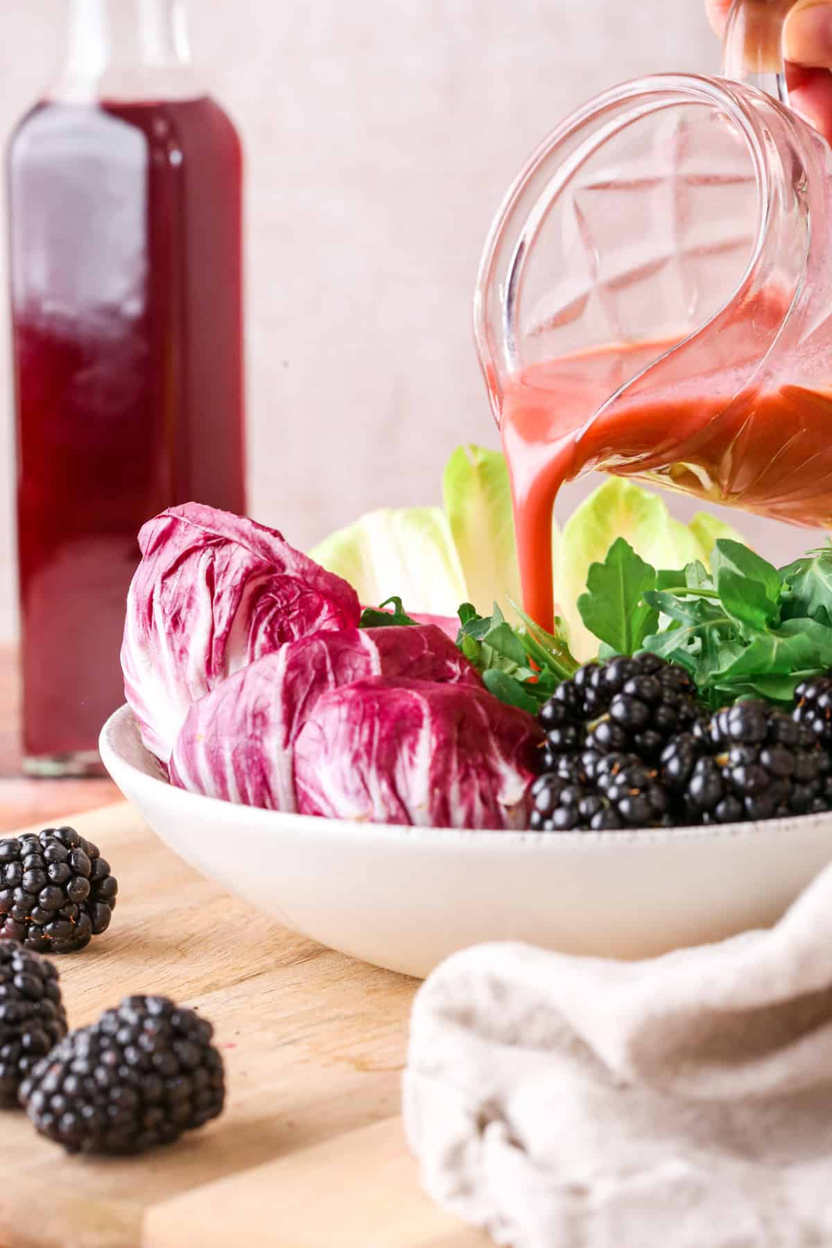 Beautifully pink salad dressing made from blackberry vinegar pouring into bowl of salad.