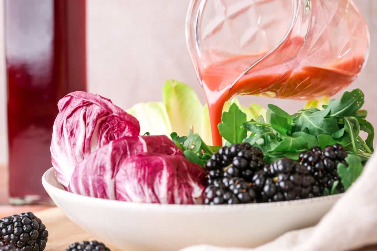 Beautifully pink salad dressing made from blackberry vinegar pouring into bowl of salad.