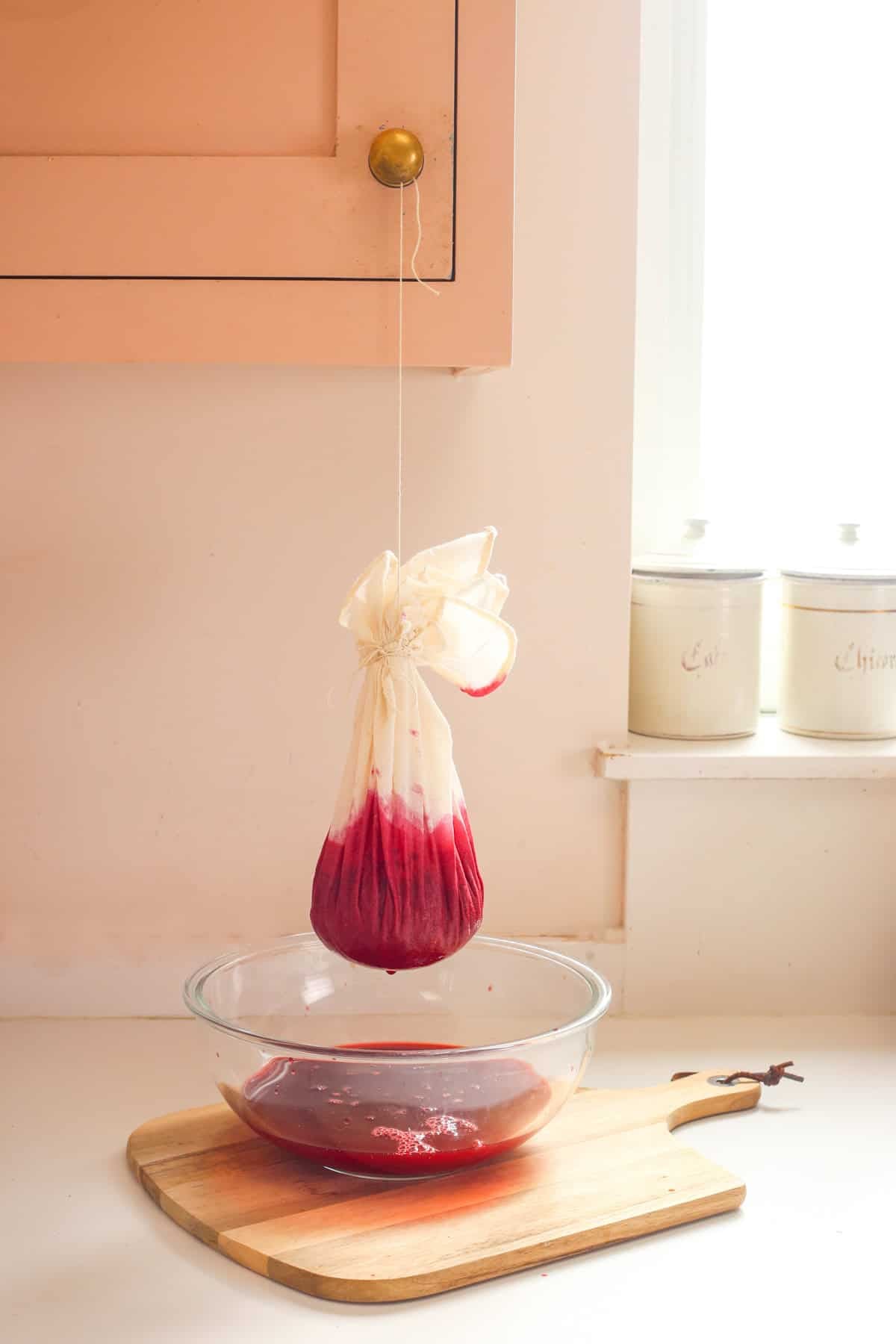 Straining bag filled with crushed blackberries and vinegar hung up on door handle and draining over a bowl.