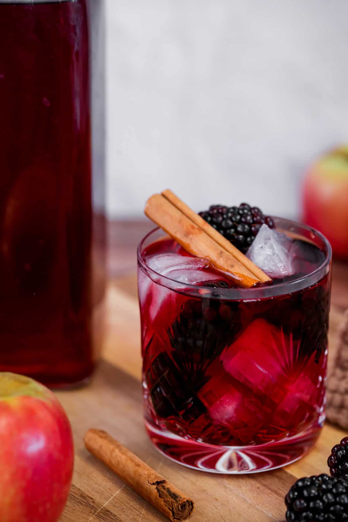 Glass of Homemade Blackberry Apple Crumble Vodka filled with ice, blackberries and a cinnamon stick.