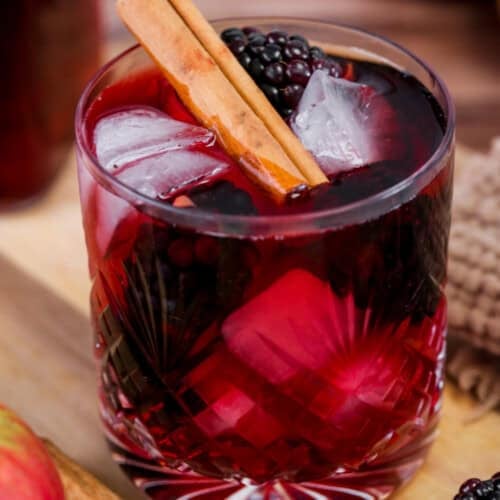 Glass of Homemade Blackberry Apple Crumble Vodka filled with ice, blackberries and a cinnamon stick.