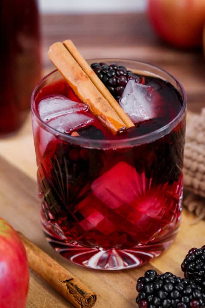 Glass of Homemade Blackberry Apple Crumble Vodka filled with ice, blackberries and a cinnamon stick.