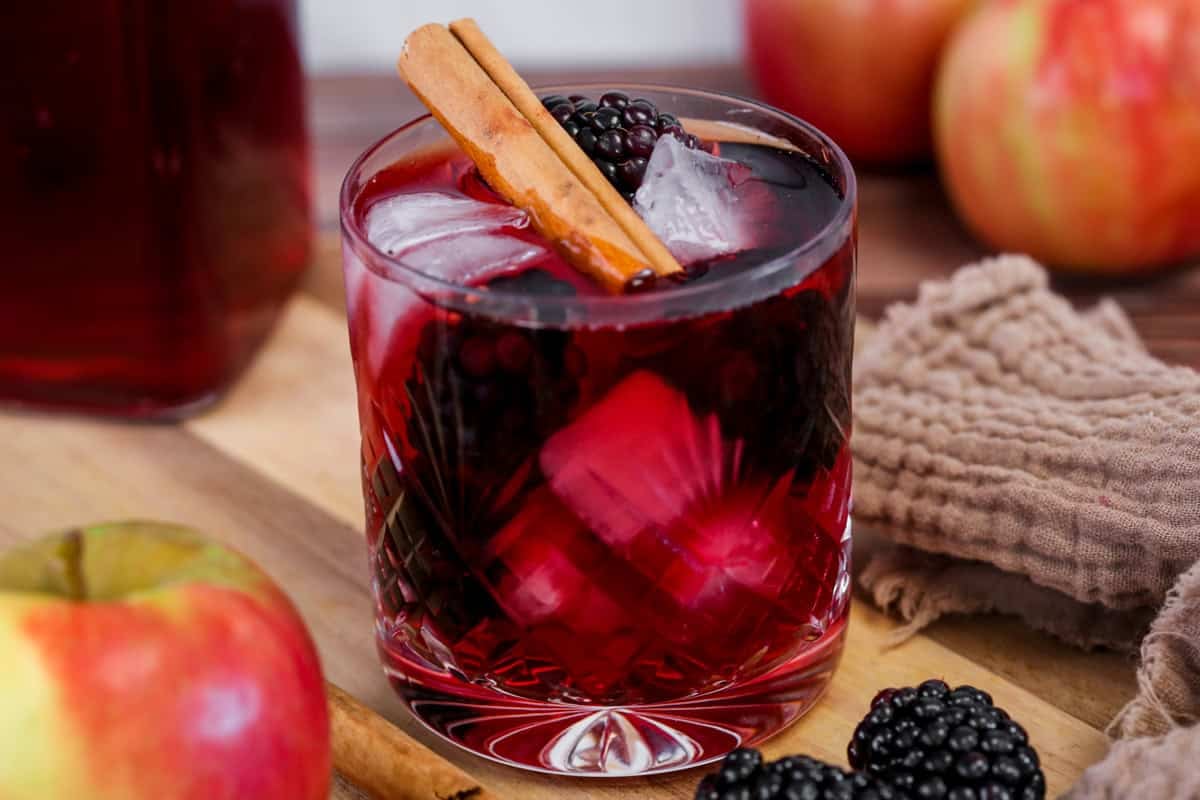 Glass of Homemade Blackberry Apple Crumble Vodka filled with ice, blackberries and a cinnamon stick.