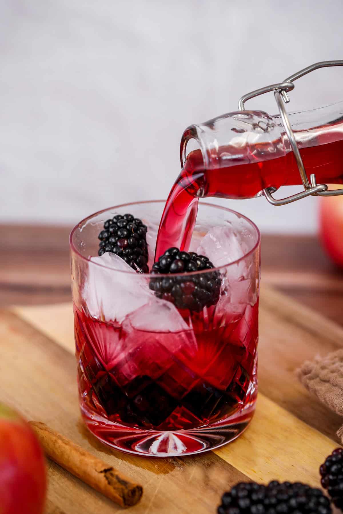 Vodka poured from bottle into a glass over ice and blackberries.