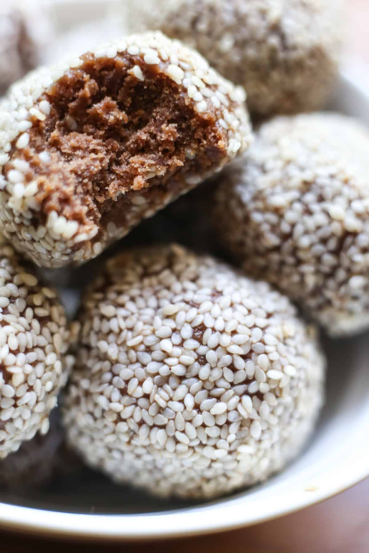 Bowl of Chocolate Tahini Date Energy Balls with bite taken out showing fudgy texture.