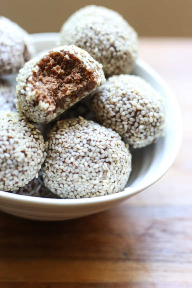 Bowl of Chocolate Tahini Date Energy Balls with bite taken out so one showing fudgy texture.