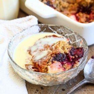 Bowl of Gluten-Free Blackberry Apple Sponge Pudding drenched in custard.
