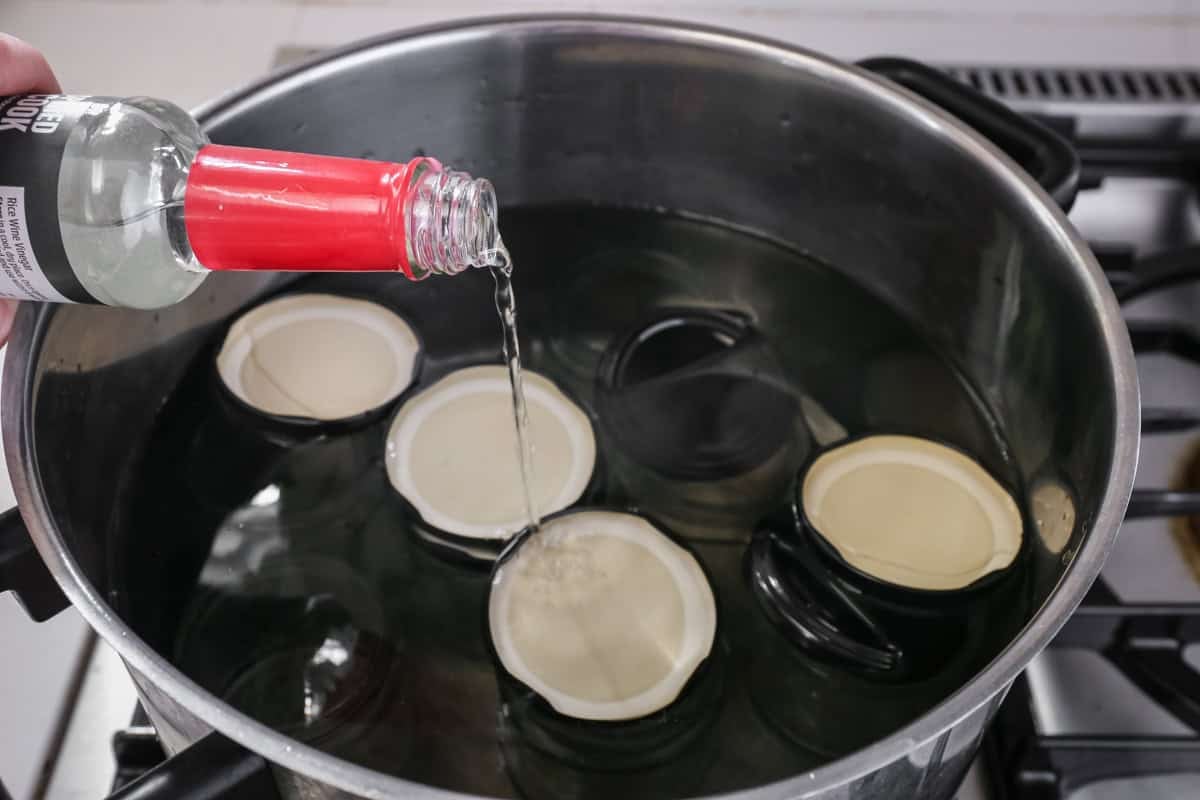 Vinegar poured into pot which is heat treating lids through the boiling-water bath method.