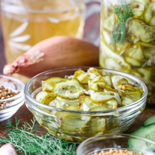 A small bowl of of pickled cucumber and shallot surrounded by the ingredients of the bread and butter pickles.