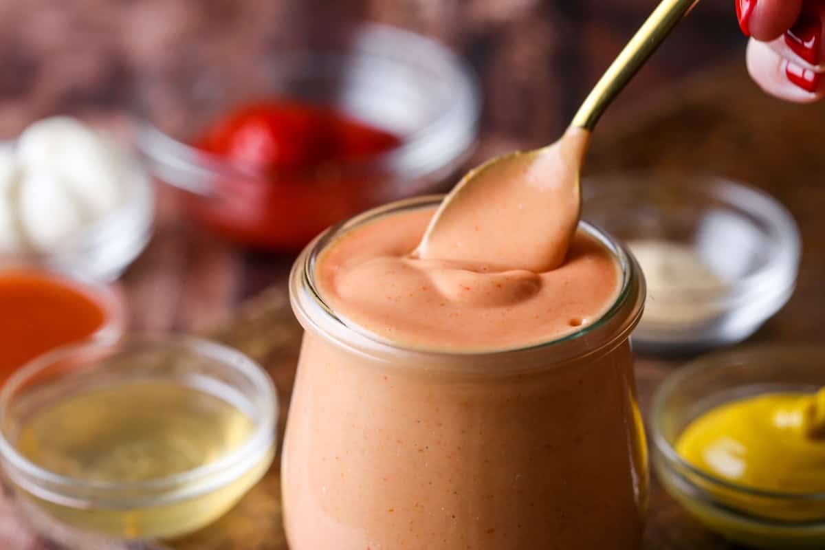Spoon dipping into a jar of thick and creamy burger sauce.