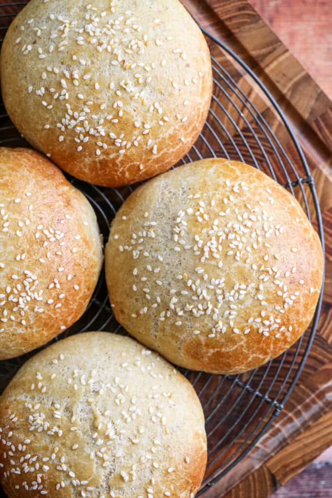 Burger Buns on wire rack cooling, golden brown and scattered with sesame seeds.
