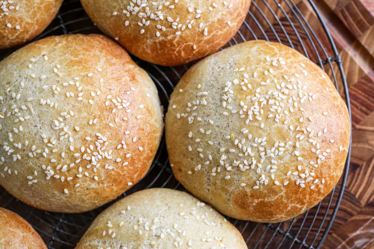 Burger Buns on wire rack cooling, golden brown and scattered with sesame seeds.