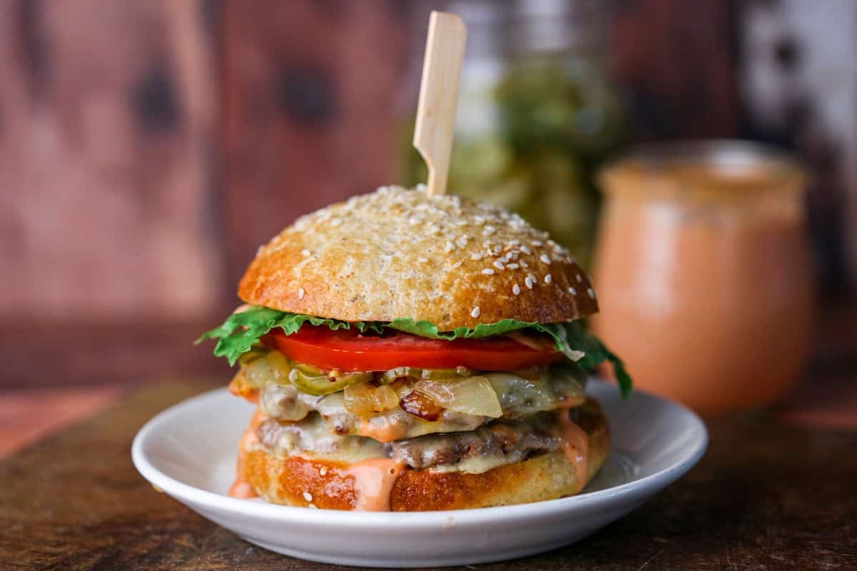 Stacked gluten-free smash burger with all the toppings, held together with wooden skewer.