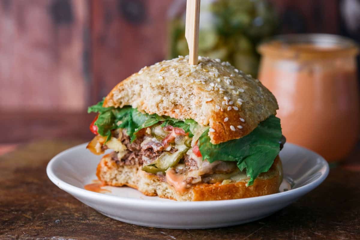 Bites taken out of gluten-free smash burger showing all the layers and toppings. Juicy and loaded.